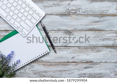 Home office workspace with computer keyboard, blank paper clipboard and green plant on wooden background. Flat lay, top view. Working home concept.