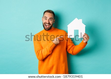 Real estate concept. Happy man pointing finger at paper home maket and smiling, standing over light blue background