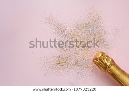 Champagne bottle and glitter on pink background with copy space. Top view, flat lay. Celebration concept