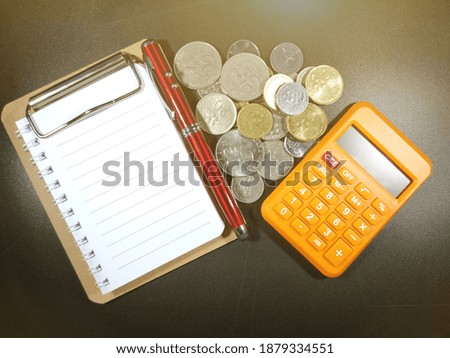 Picture of a Business Money Concept Idea.Notebook,pen and coins with black and soft flare background.