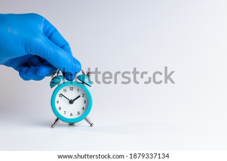 medic person holding alarm clock over grey background. copy space. studio shot. minimal. medicine time concept. Royalty-Free Stock Photo #1879337134