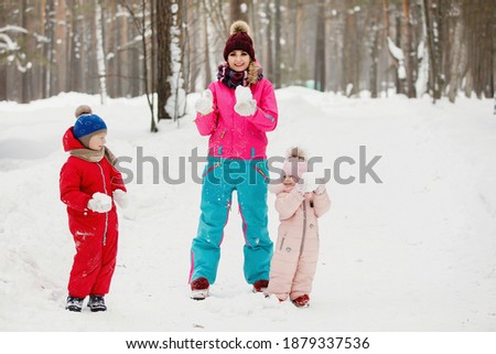 Mom, son and daughter in winter clothes are having fun, people are playing in the snow. Warm blue, pink and red jackets, knitted hats. Family happiness, values and traditions. Selective focus.