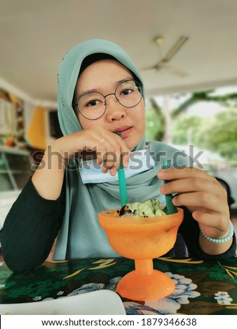 Selective focus photo with noise effect of young girl enjoying eating dessert bean ice or locally known as Aiskrim Cendol Gula Apong.
