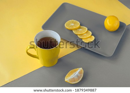 Yellow cup of tea and sliced lemon on gray plate. Trendy colors 2021.