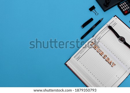 Modern office desk workplace with blank notebook, pen and supplies. Copy space on blue background. Top view. Flat lay style. Lettering Thursday. High quality photo