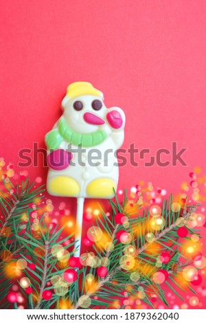 Snowman made of sugar candies. Fir branch with decorative bokeh. Merry Christmas and happy New Year greeting card. Lollipops of funny snowman Christmas present. Red background          