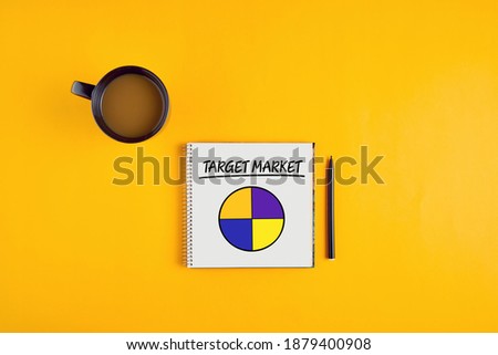 The word target market and a pie chart on notebook with pen and coffee mug on yellow background.