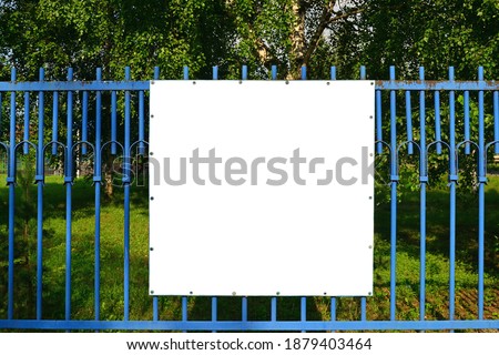 Mock up blank white banner on blue metal fence against green vegetation background