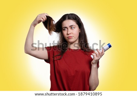 Portrait of a young woman holding a shampoo and looking at her dry hair tips. The concept of dandruff, dryness and hair care