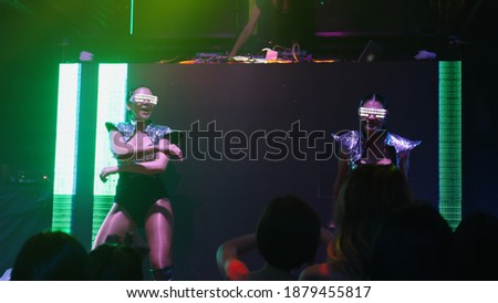 Group of people dance in disco night club to the beat of music from DJ on stage . New year night party and nightlife concept .