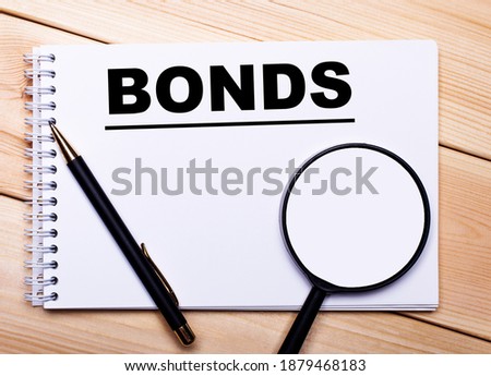 On a light wooden background lie a pen, a magnifying glass and a notebook with the text BONDS