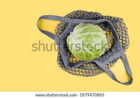A head of cabbage lies in an ecological string bag on a yellow background. Eco friendly shopping, environmental protection concept. Colors of the Year 2021. Illuminating yellow and ultimate gray.