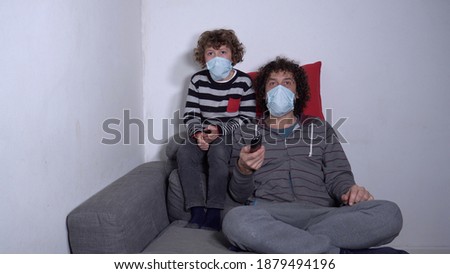 Europe, Italy , Milan - Father and son child boy 6 years old watching television and playing video games with mask during Covid-19 Coronavirus lockdown quarantine home