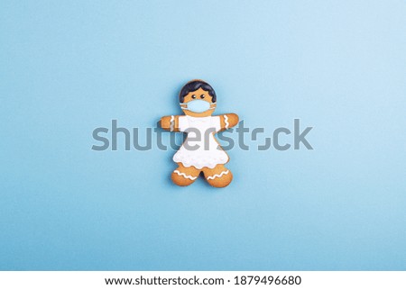 a gingerbread girl with dark hair and a white dress wearing a medical mask. the concept of a pandemic coronavirus, mandatory wearing of masks