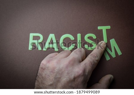 Human fingers sliding a letter to the word Racism to make it Racist, written with plastic letters on a brown paper background, concept
