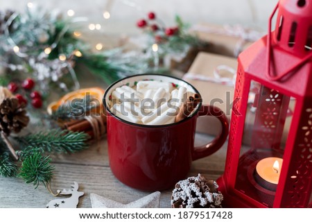 Winter hot drink, cacao with marshmallows and cinnamon or spicy hot chocolate in red cup and Christmas garland. Festive vintage background.