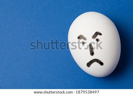 Egg with an angry face, on blue background with copy space.