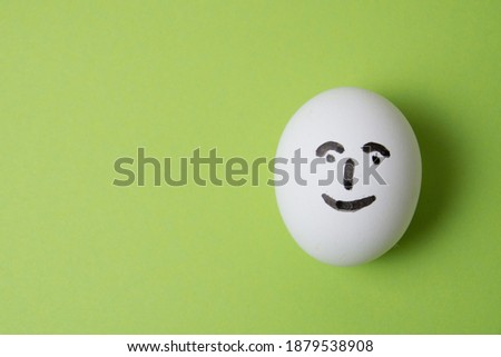 Egg with a cheerful and joyful face, on a green background with copy space
