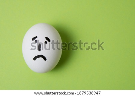 Egg with a sad face, on a green background with copy space