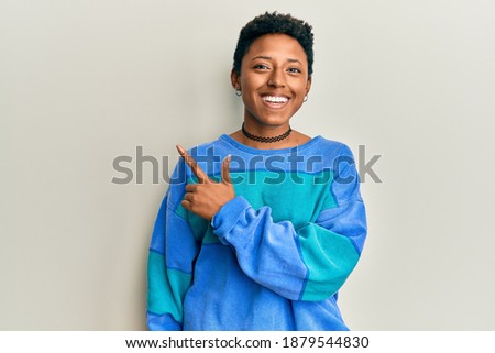 Young african american girl wearing casual clothes smiling cheerful pointing with hand and finger up to the side 