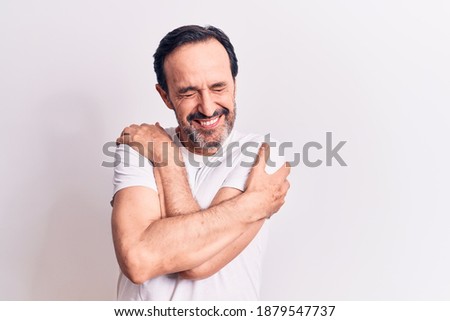 Middle age handsome man wearing casual t-shirt standing over isolated white background hugging oneself happy and positive, smiling confident. Self love and self care