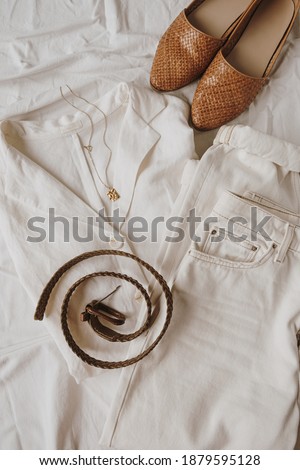 Fashion concept with female clothes and accessories on white linen. Leather slippers, belt, white jeans, blouse, golden necklace. Flat lay, top view lifestyle fashion minimalist blogger composition.