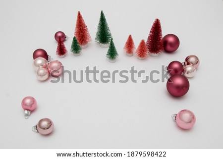 Green, red and orange plastic artificial Christmas trees and Christmas balls on white backdrop