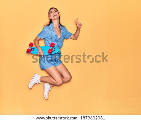 Young beautiful girl holding skate smiling happy. Jumping with smile on face doing victory sign over isolated yellow background