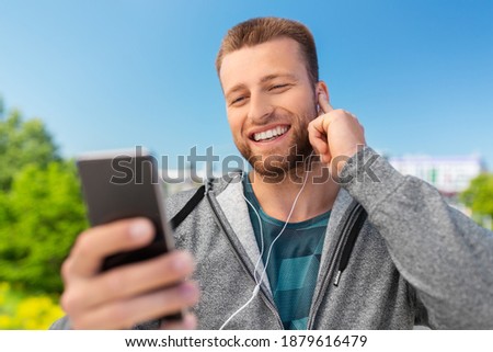 fitness, sport and technology concept - happy smiling young man with earphones and smartphone listening to music outdoors