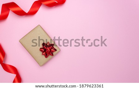 Gift box and red satin ribbon on the side on a pink background. Free space for text. Holidays, Christmas, Valentine's Day.