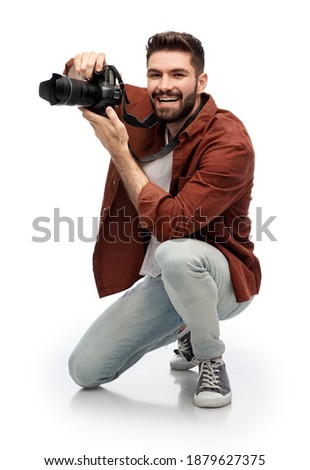 photography, profession and people and concept - happy smiling man or photographer with digital camera staying on one knee and taking picture over white background