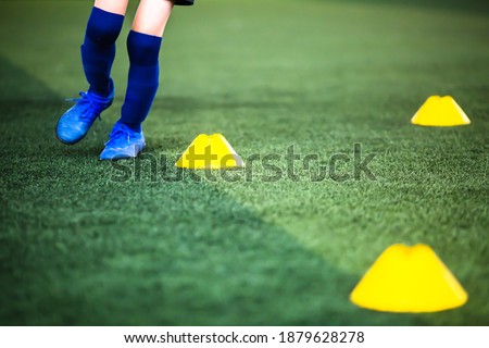 Selective focus to cone marker with blurry boy soccer player is jogging on green artificial turf. Material for training class of football academy.