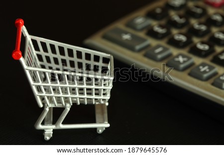 Miniature shopping cart model see calculator as a background scene represent online shopping and retail business concept related idea.
