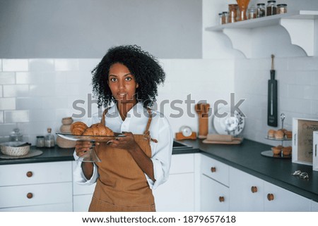 Holds croissants. Young african american woman with curly hair indoors at home.