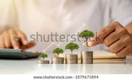 A businessman holding a coin with a tree that grows and a tree that grows on a pile of money. The idea of maximizing the profit from the business investment. Royalty-Free Stock Photo #1879675894