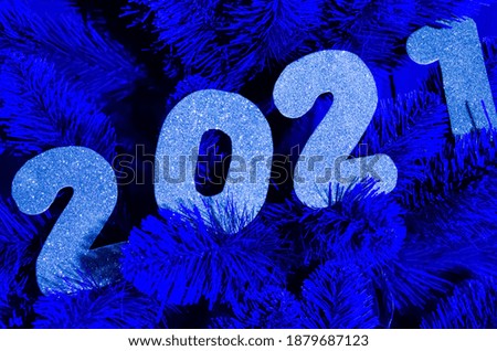 Happy New Year 2021 winter holiday greeting card. Blue shiny numbers 2021 on blue Christmas tree. Neon numbers. New year concept. 2021 happy new year background with metallic silver colored numbers.