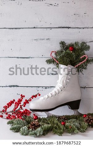 winter composition with figure skates and fir branches on the background of a white aged wooden wall.