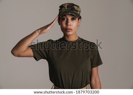 Confident african american soldier woman saluting and looking at camera isolated over grey wall