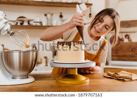 Beautiful pleased pastry chef woman making cake with chocolate cream at cozy kitchen Royalty-Free Stock Photo #1879707163