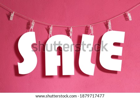 White, paper cut sale sign hanging on a clothesline over a vivid pink - magenta wall background.  Royalty-Free Stock Photo #1879717477