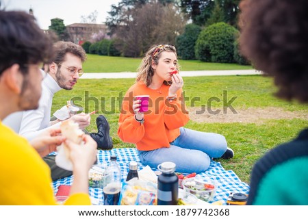 Four multiethnic friends having picnic in a park in group having fun celebrating and eating food enjoying living together and good company