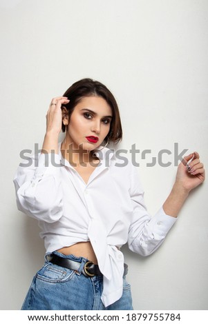 Young hipster girl wearing blue jeans and blank white t-shirt with empty area for your logo or design, mock-up of white cotton t-shirt, white wall in the background