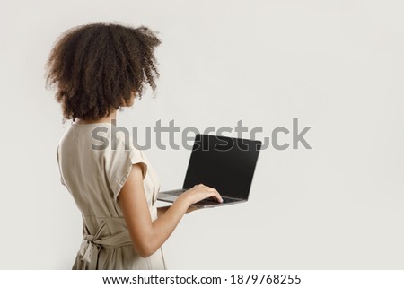 Blogger or freelancer works online at home. Millennial african american lady student with curly hair in casual typing on laptop with blank screen, back, isolated on light background, free space