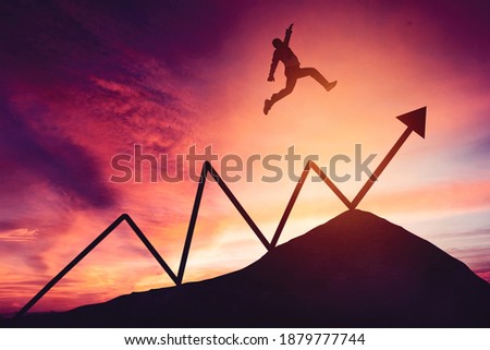 Silhouette of businessman jumping above upward arrow on the peak of mountain with dawn sky background
