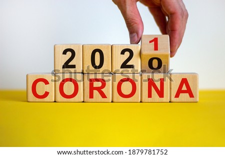 Covid-19 pandemic in 2021 symbol. Male hand flips a wooden cube and changes words 'corona 2020' to 'corona 2021'. Beautiful yellow table, white background, copy space. 2021 corona concept.