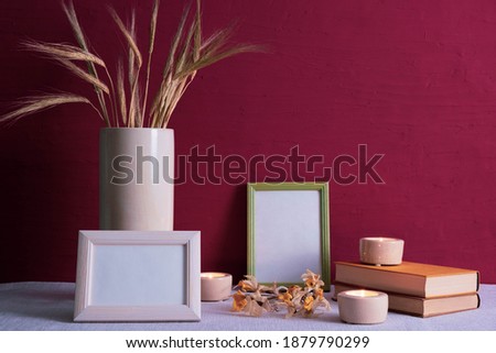 old books, candles are burning, white vase with ears of wheat, photo frames on a red background on the table