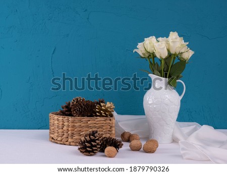 white vase with white roses, near walnuts on a blue background on the table