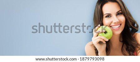 Portrait of toothy smiling happy woman holding green apple, isolated over grey color background. Brunette girl at optimistic, positive, dieting or dental health care, stomatology concept. Wide image.