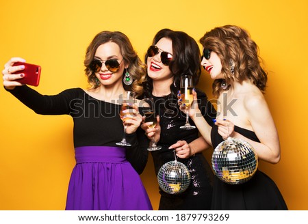 Celebration, party, and people concept - three fashionable young women drinking champagne and taking a selfie.