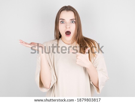 Happy young woman standing isolated over white wall background. Looking camera showing copyspace pointing.